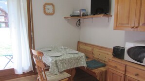 A dining area with a table set for four, a wooden chair, a clock on the wall, a television on a shelf, and a microwave on the counter. - Studio for 4 at Contamines with terrace and parking (Les Contamines-Montjoie)