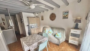 A compact living space with a kitchenette, a dining area with a table and chairs, a sofa with cushions, a clock on the wall, and a lamp on a side table.