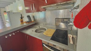 A compact kitchen with a double sink, a stove, and red cabinets.