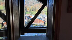Vista da una finestra con cornice in legno, su una cittadina con edifici e una collina boscosa.