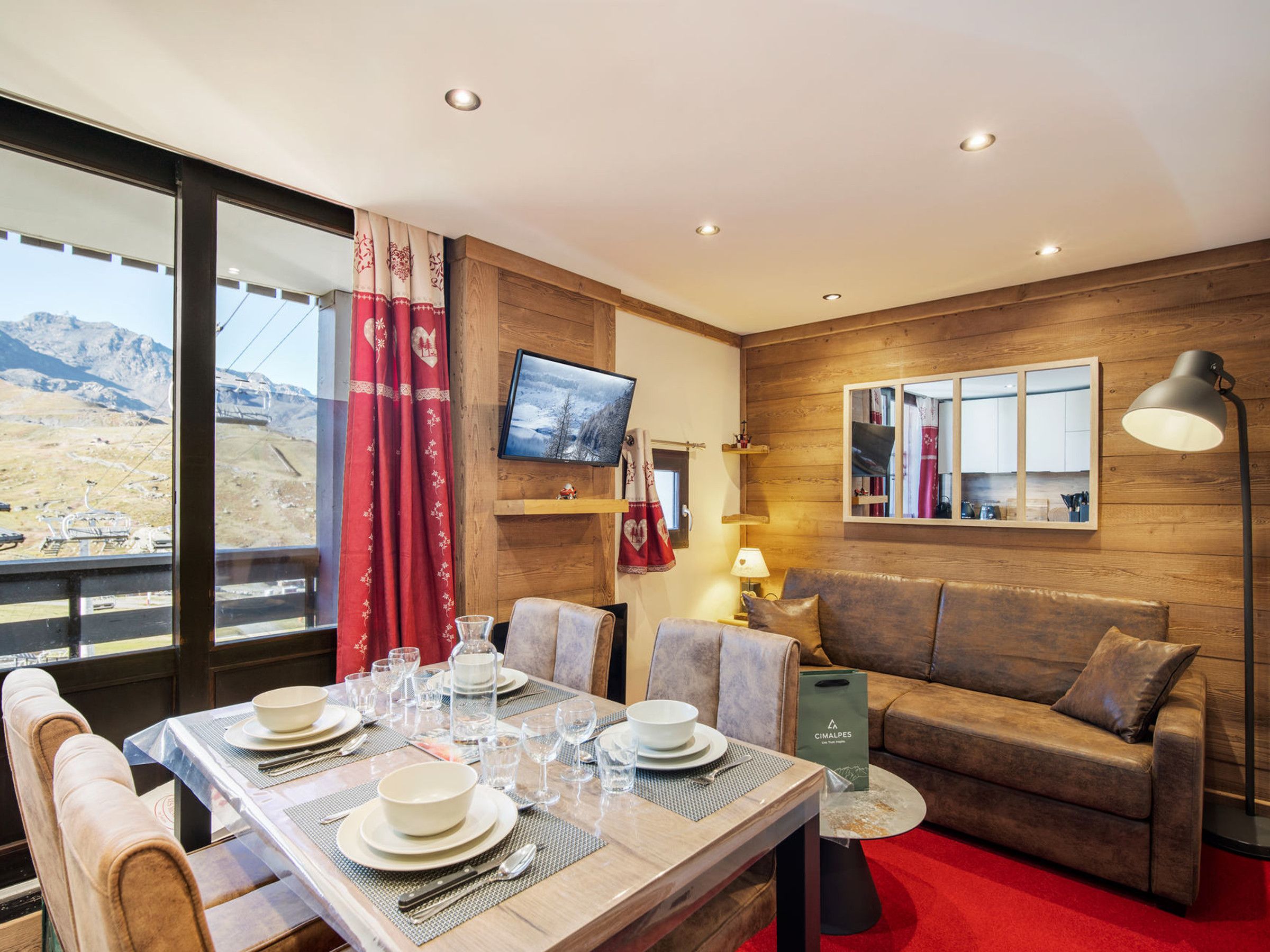 Un coin repas avec une table dressée pour quatre personnes, un canapé, un téléviseur et une vue sur les montagnes.