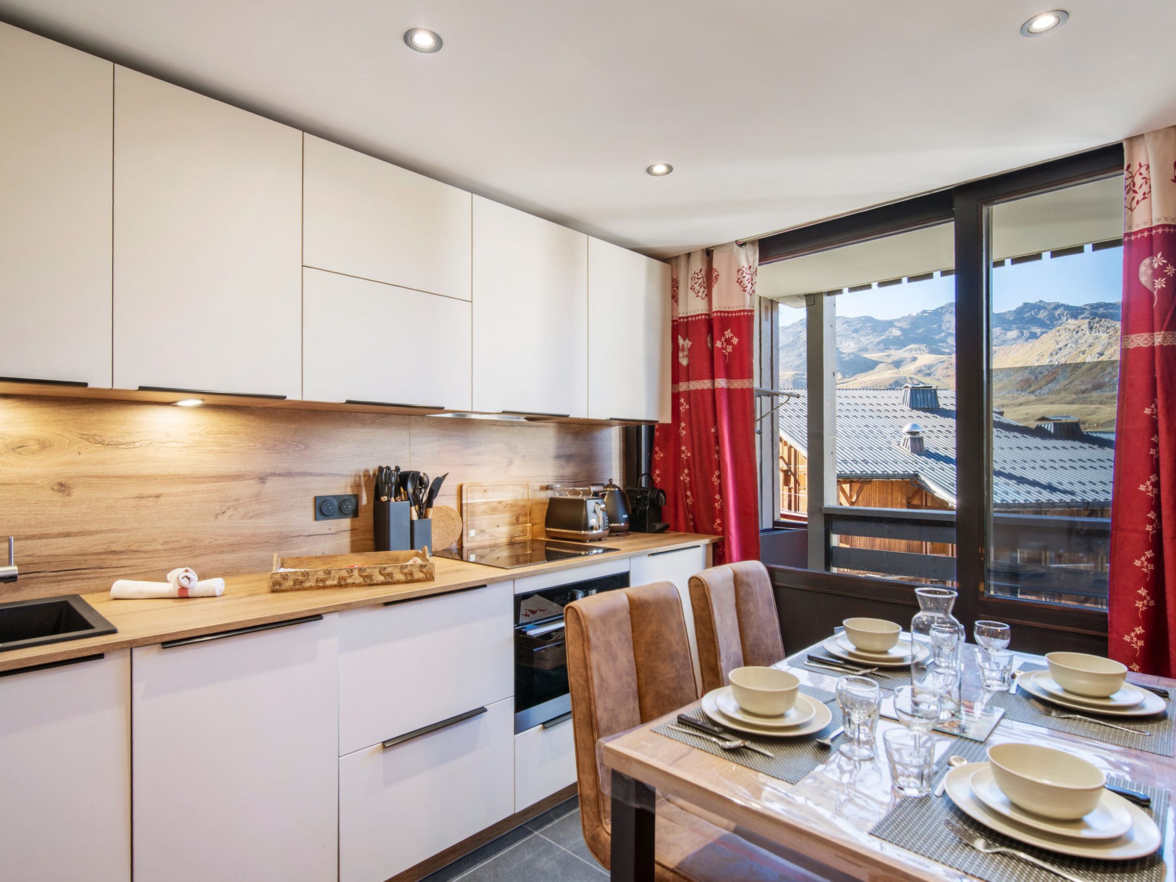 A modern kitchen with white cabinets, a wooden countertop, and a dining area with a table set for four.