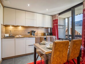 A modern kitchen with built-in cabinets, a dining area with a table set for two, and a view of the mountains through large windows. - Ski-in/Ski-out Apartment in Val Thorens with WIFI (Val Thorens)