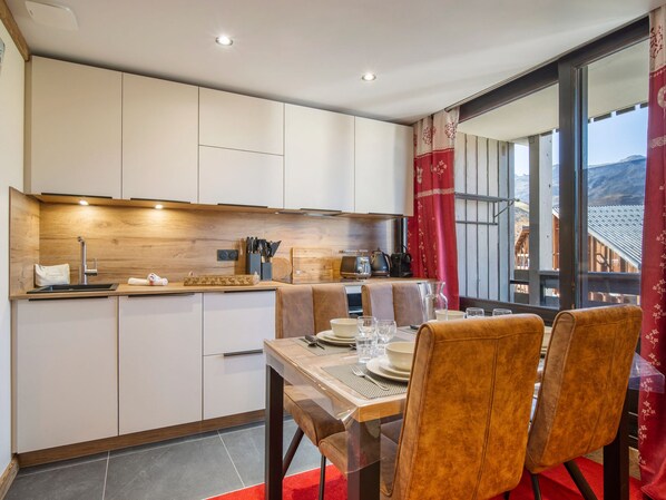 A modern kitchen with built-in cabinets, a dining area with a table set for two, and a view of the mountains through large windows. - Ski-in/Ski-out Apartment in Val Thorens with WIFI (Val Thorens)