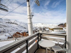 Ein Balkon mit Blick auf eine verschneite Berglandschaft, eine Seilbahn und ein modernes Gebäude mit gewundener Fassade.