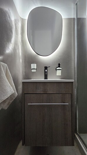 A bathroom with a round mirror, two wall-mounted lights, a black faucet, and a wooden vanity. - Mykonos4Islands Villa "Athena" with shared pool - 5 min walking from the beach (MYKONOS)