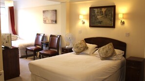Ein Hotelzimmer mit einem großen Bett, zwei Nachttischlampen, einem Bild an der Wand, einem Schreibtisch mit Computer und einem Sessel.