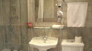 Ein Badezimmer mit Duschkabine aus Glas, einem Standwaschbecken, einer Toilette und einem Ablagefächer aus Glas mit Toilettenartikeln.