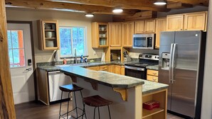A modern kitchen with wooden cabinets, a stainless steel refrigerator, and a granite countertop. - Secluded 3 bed house in Kila with flowing creek, hot tub, with plenty of parking (Kila)