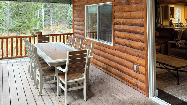 A wooden cabin with a deck, a dining area with chairs and a table, and a living room with a sofa and a coffee table. - Secluded 3 bed house in Kila with flowing creek, hot tub, with plenty of parking (Kila)