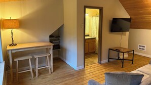 A cozy room with a wooden ceiling, a TV mounted on the wall, a small table with a lamp, and a sofa. - Secluded 3 bed house in Kila with flowing creek, hot tub, with plenty of parking (Kila)