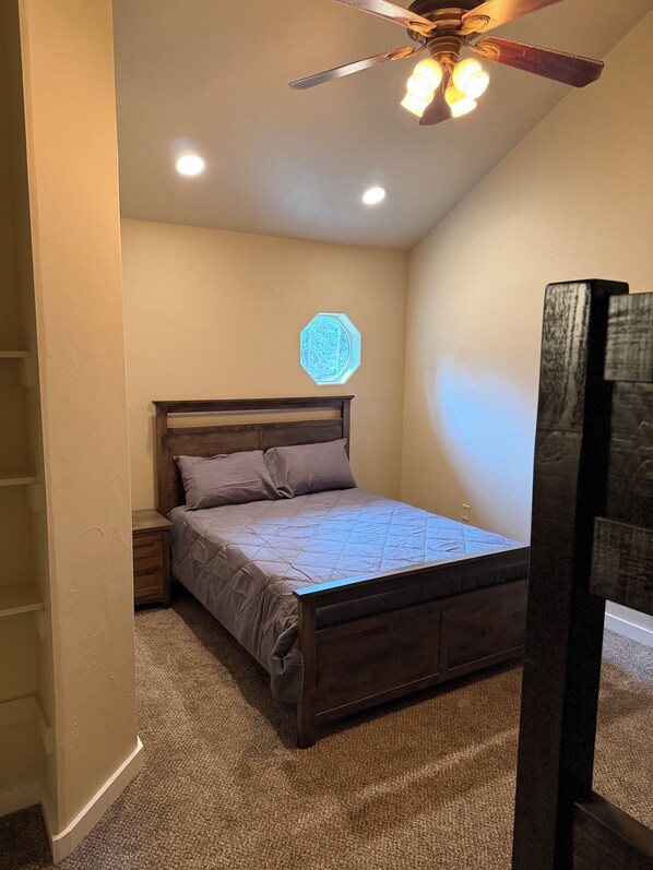 A bedroom with a wooden bed, a ceiling fan, recessed lighting, and a decorative wall piece. - Secluded 3 bed house in Kila with flowing creek, hot tub, with plenty of parking (Kila)