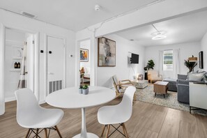 Ein modernes Wohnzimmer mit einem runden Tisch, zwei weißen Stühlen, einem grauen Sofa und einem Fernseher.