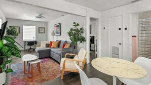 Een moderne woonkamer met een grijze bank, een witte fauteuil, een ronde tafel en een kleurrijk vloerkleed.