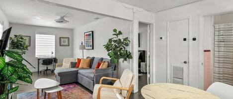 Un salon moderne avec un canapé gris, un fauteuil blanc, une table ronde et un tapis coloré.