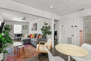 Ein modernes Wohnzimmer mit grauem Sofa, einem weißen Sessel, einem runden Tisch und einem farbenfrohen Teppich.