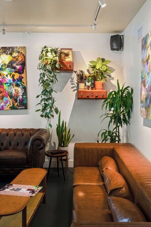Ein Wohnzimmer mit einem braunen Ledersofa, einem kleinen runden Tisch und einem Couchtisch. Es gibt Blumentöpfe und ein Bild an der Wand.