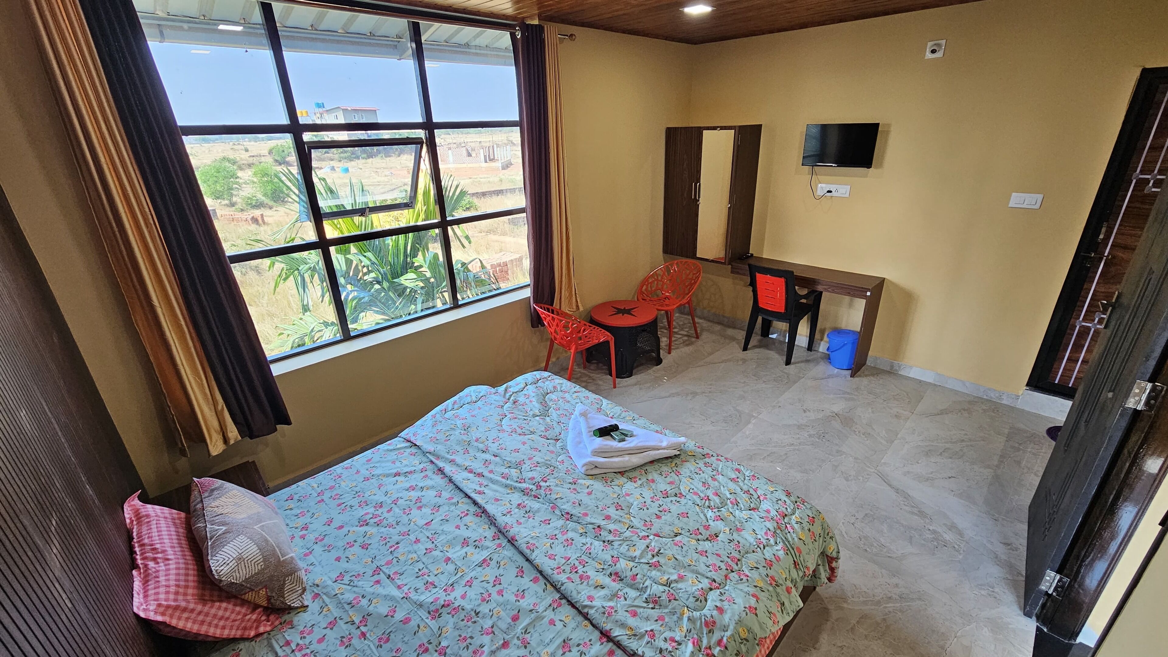 Quarto com cama, escrivaninha, televisão e janela com vista para o exterior.