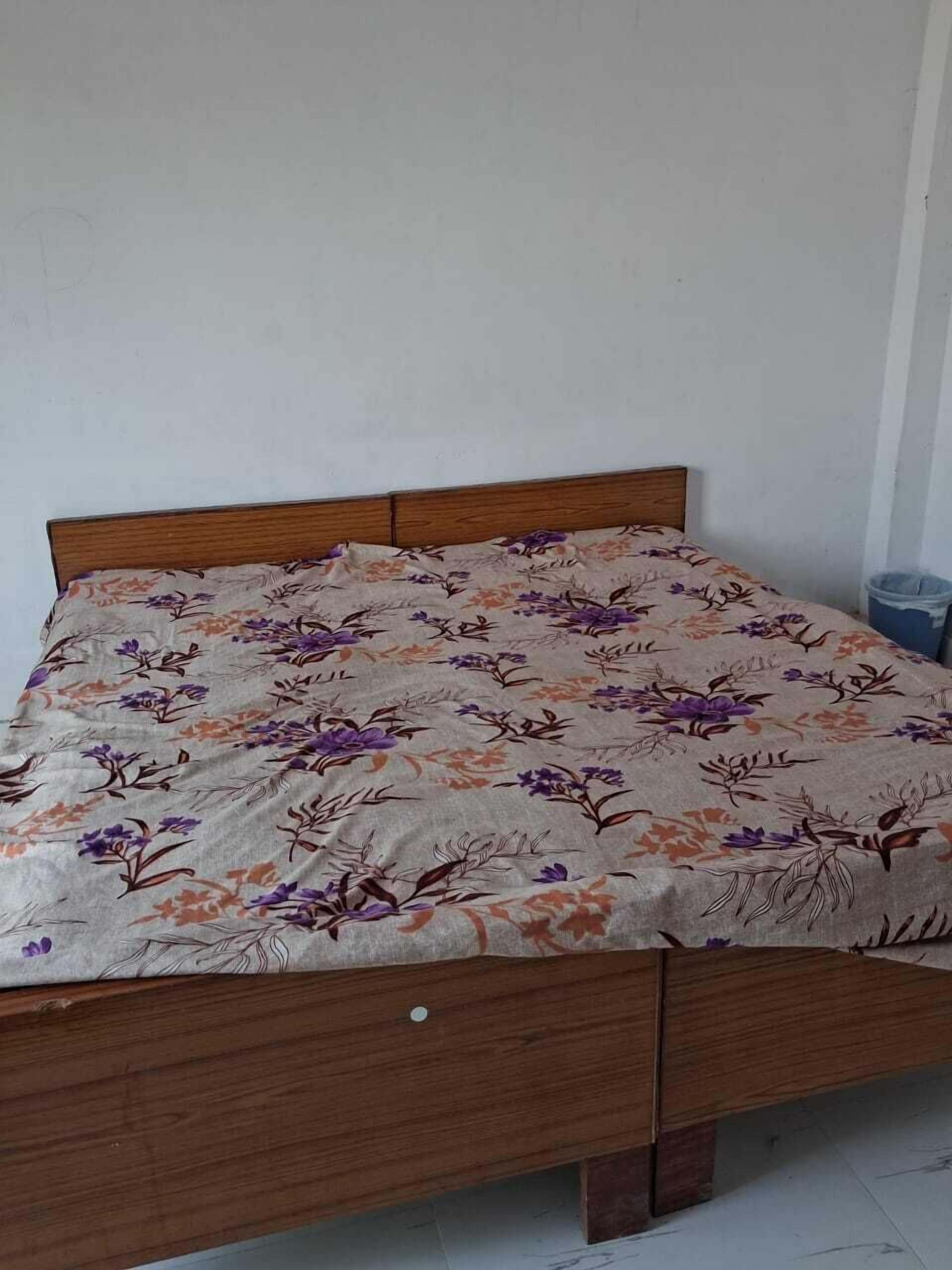 Un lit avec une couvre-lit à motifs floraux, une tête de lit en bois et un petit tiroir.