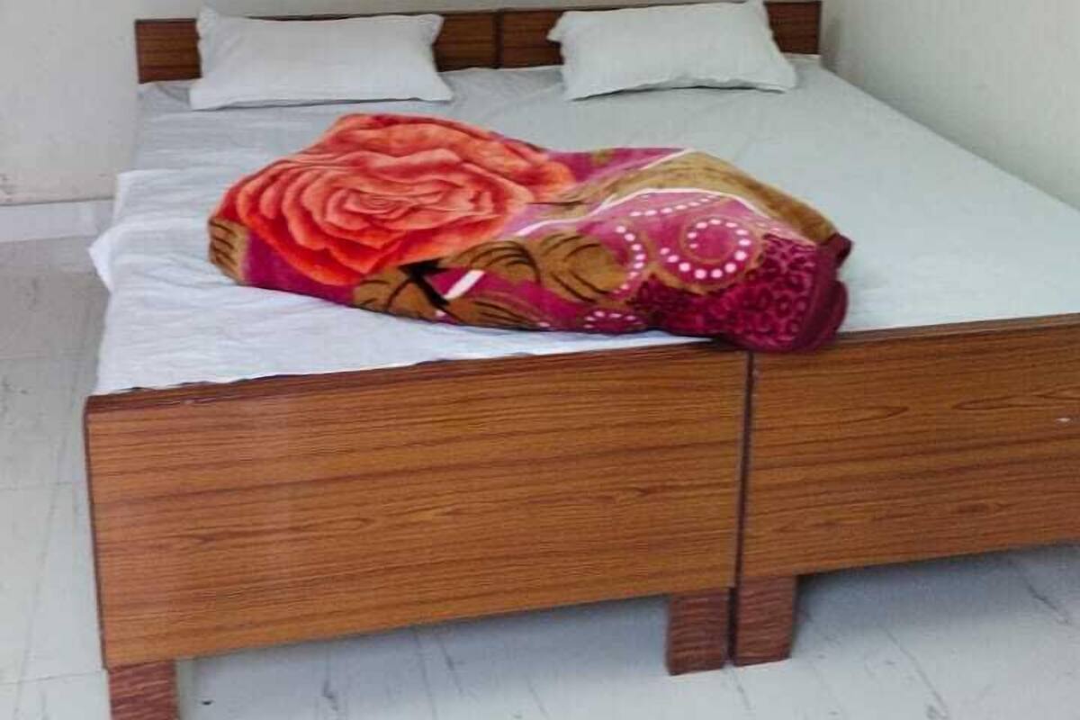 A single bed with a wooden frame, white bedding, and a colorful blanket.