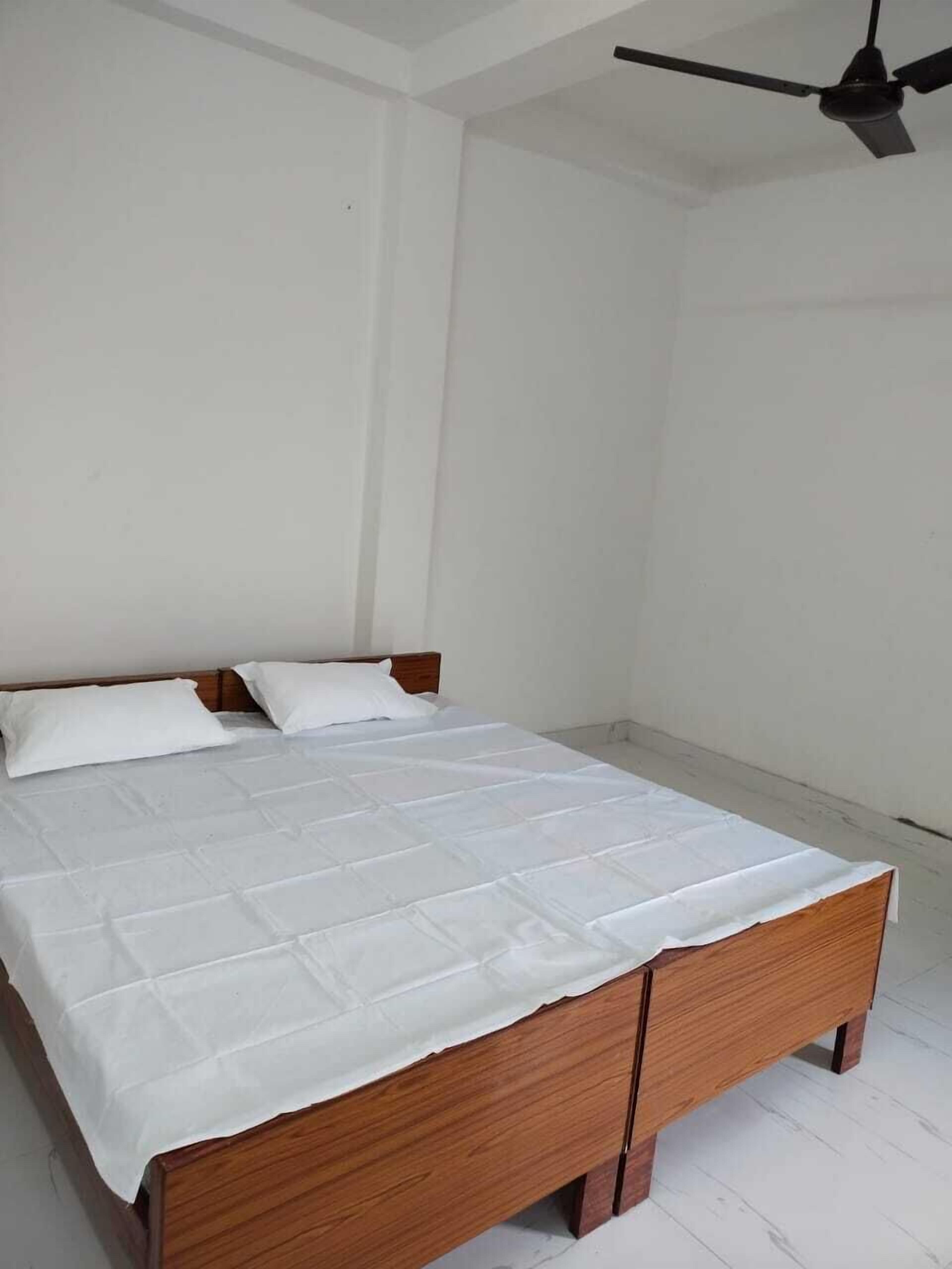 A single bed with a wooden frame and white bedding in a room with white walls and a ceiling fan.