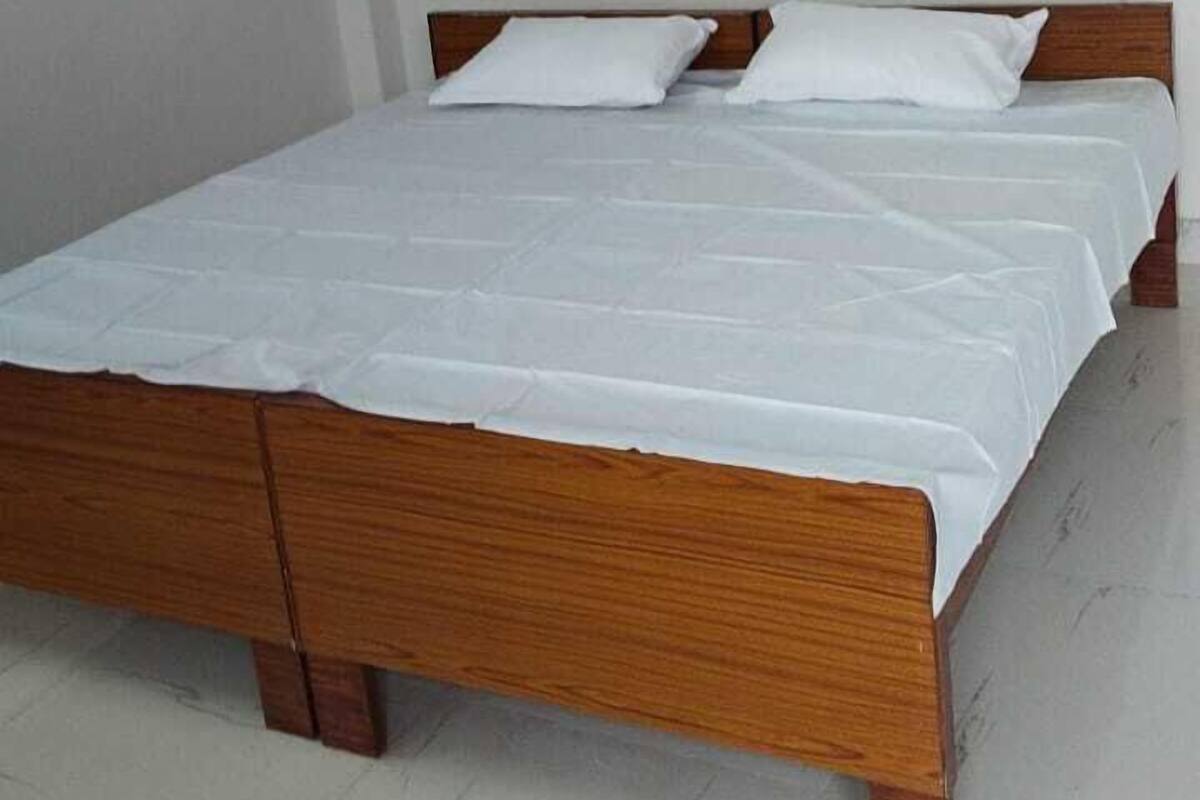 A single bed with a wooden frame and white bedding in a room with white walls and a tiled floor.