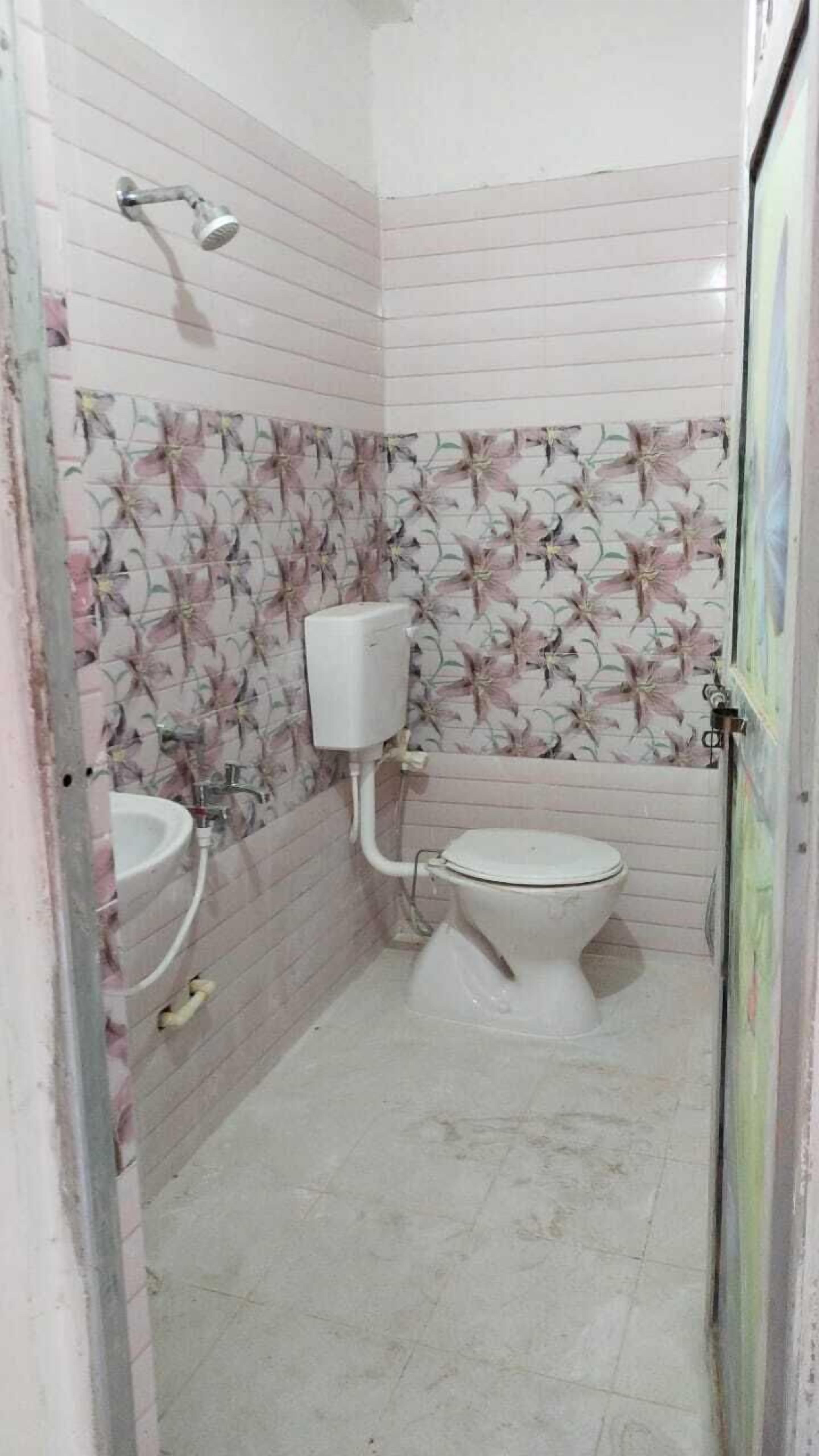 A small bathroom with a toilet, a sink, and a shower. The walls are tiled with a floral pattern.