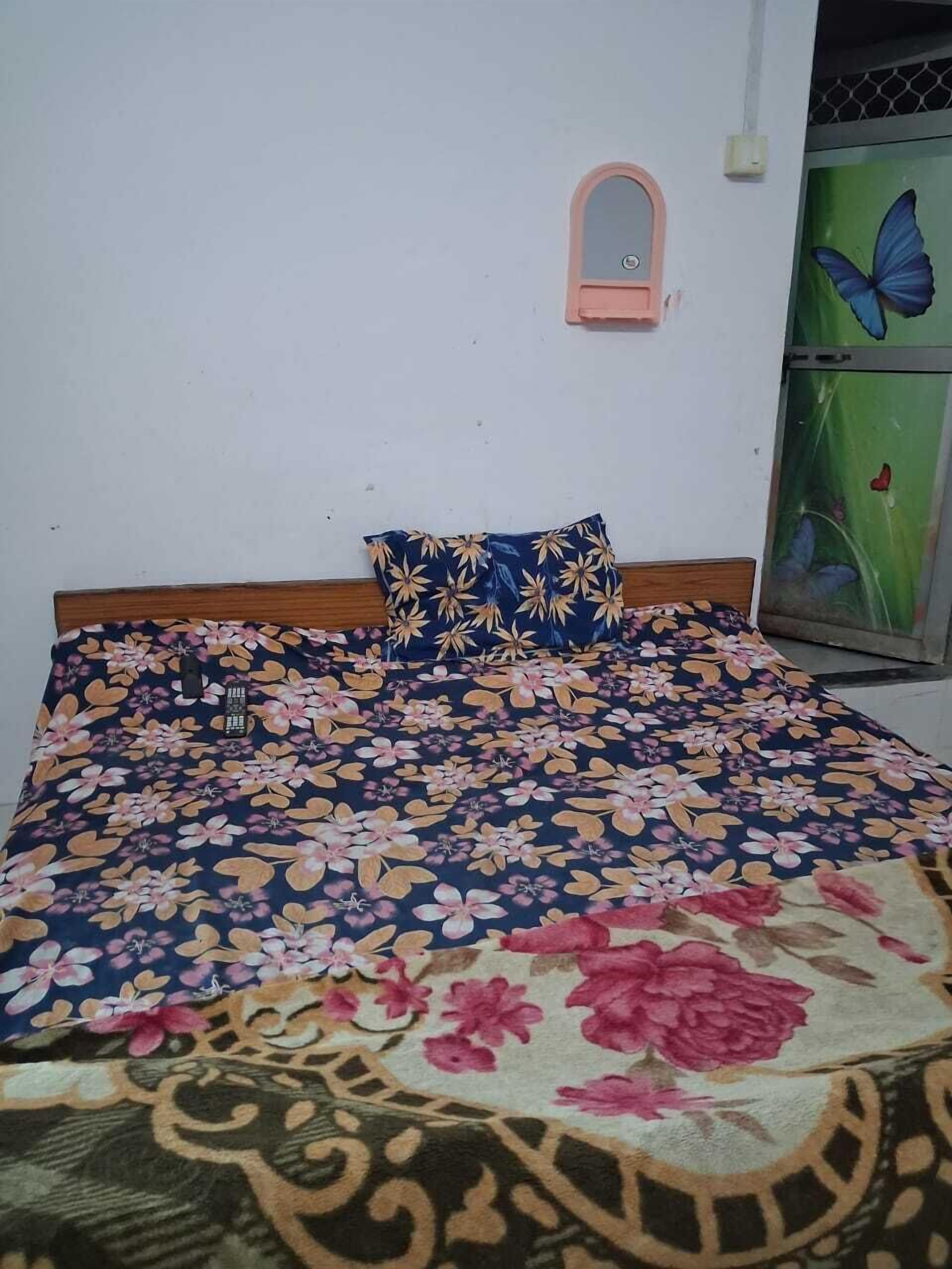 Una cama con colcha estampada, cabecera de madera y un pequeño espejo en la pared.