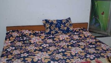 Una cama con colcha estampada, cabecera de madera y un pequeño espejo en la pared.