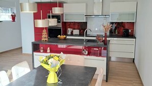 Moderni keittiö, jossa on ruokailutila, keskeinen keittiösaareke, riippuvalaisimet ja näkymä olohuoneeseen.