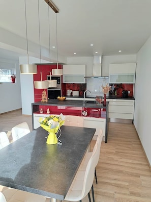 Een moderne keuken met een eethoek, met een centraal eiland, hanglampen en uitzicht op de woonkamer.