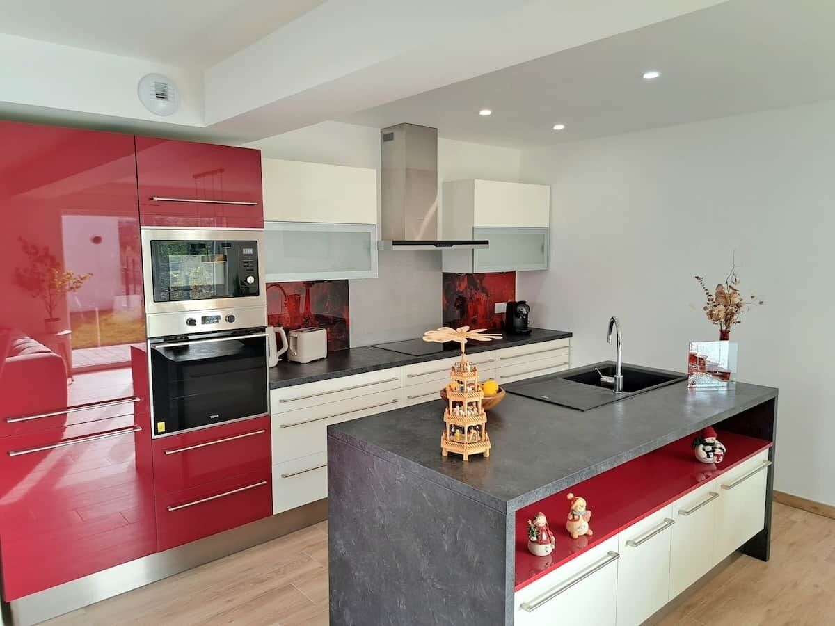 Een moderne keuken met rode kastjes, een ingebouwde oven en een centraal eiland met een spoelbak.