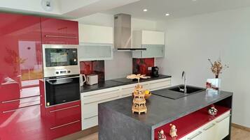 Een moderne keuken met rode kastjes, een ingebouwde oven en een centraal eiland met een spoelbak.