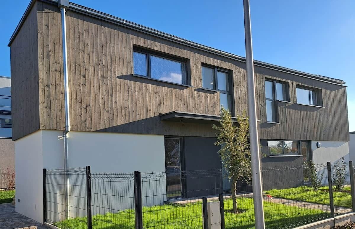 Een modern gebouw met twee verdiepingen, een plat dak, grote ramen en een omheinde tuin.