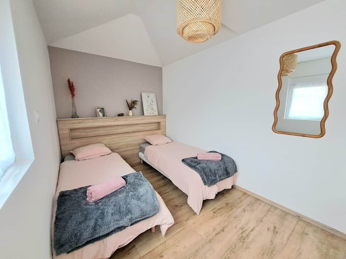 A bedroom with two beds, a wooden headboard, a mirror, and a woven light fixture.