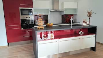 A modern kitchen with red cabinetry, a stainless steel range hood, and a central island with a reflective surface.