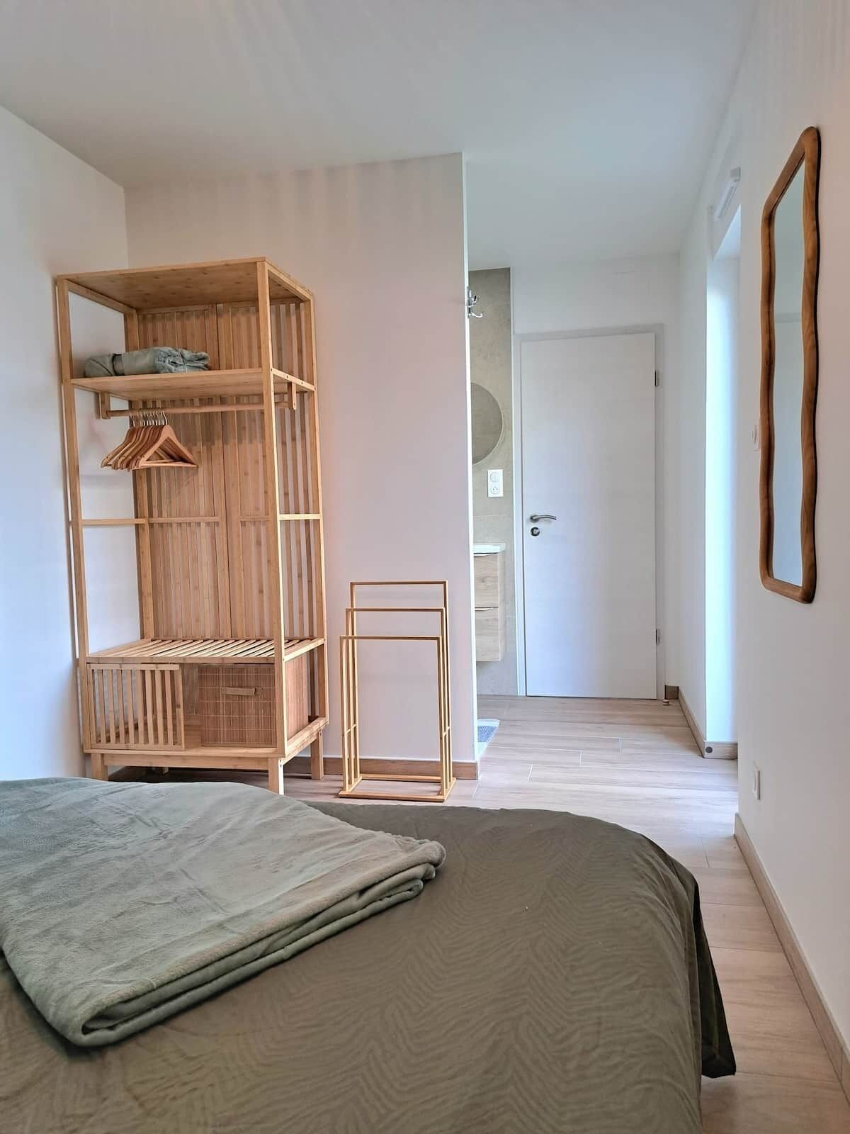 Een slaapkamer met een bed, een houten garderobe, een klein tafeltje en een deur naar een andere kamer.