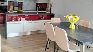 Moderni keittiö, jossa on keskeinen saareke, valkoiset kaapit ja ruokailutila, jossa on pöytä ja tuolit.