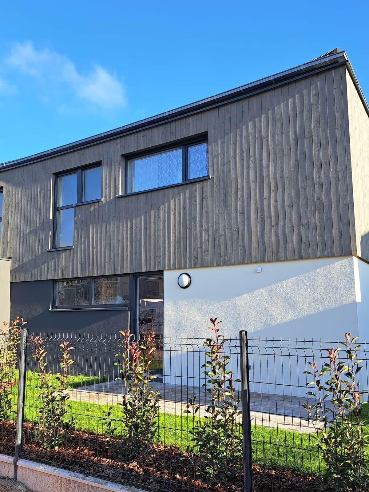 Een modern gebouw met twee verdiepingen, een plat dak, grote ramen en een zichtbare garage-ingang.