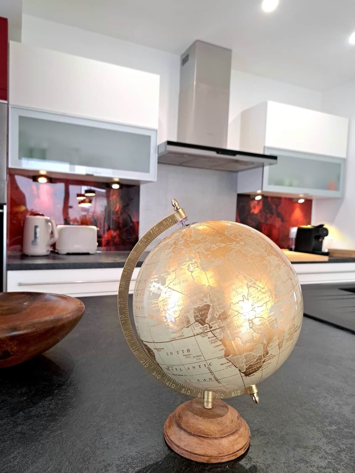 Een wereldbol op een houten voet in een moderne keuken met witte kasten en een rode achterwand.