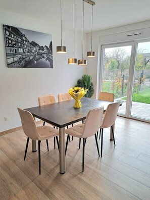 A dining area with a large table, six chairs, pendant lights, and a cityscape painting on the wall. - Chez Fernand - New home in Colmar with parking and a garden (Colmar)