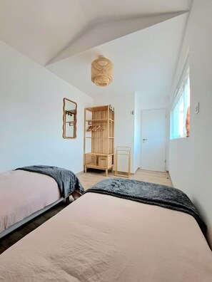 A bedroom with two beds, a wooden wardrobe, a hanging light fixture, and a door leading to another room. - Chez Fernand - New home in Colmar with parking and a garden (Colmar)