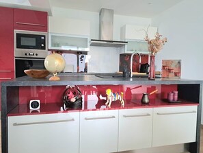 A modern kitchen with a red countertop, white cabinets, and a microwave. - Chez Fernand - New Home in Colmar with Parking and a Garden (Colmar)