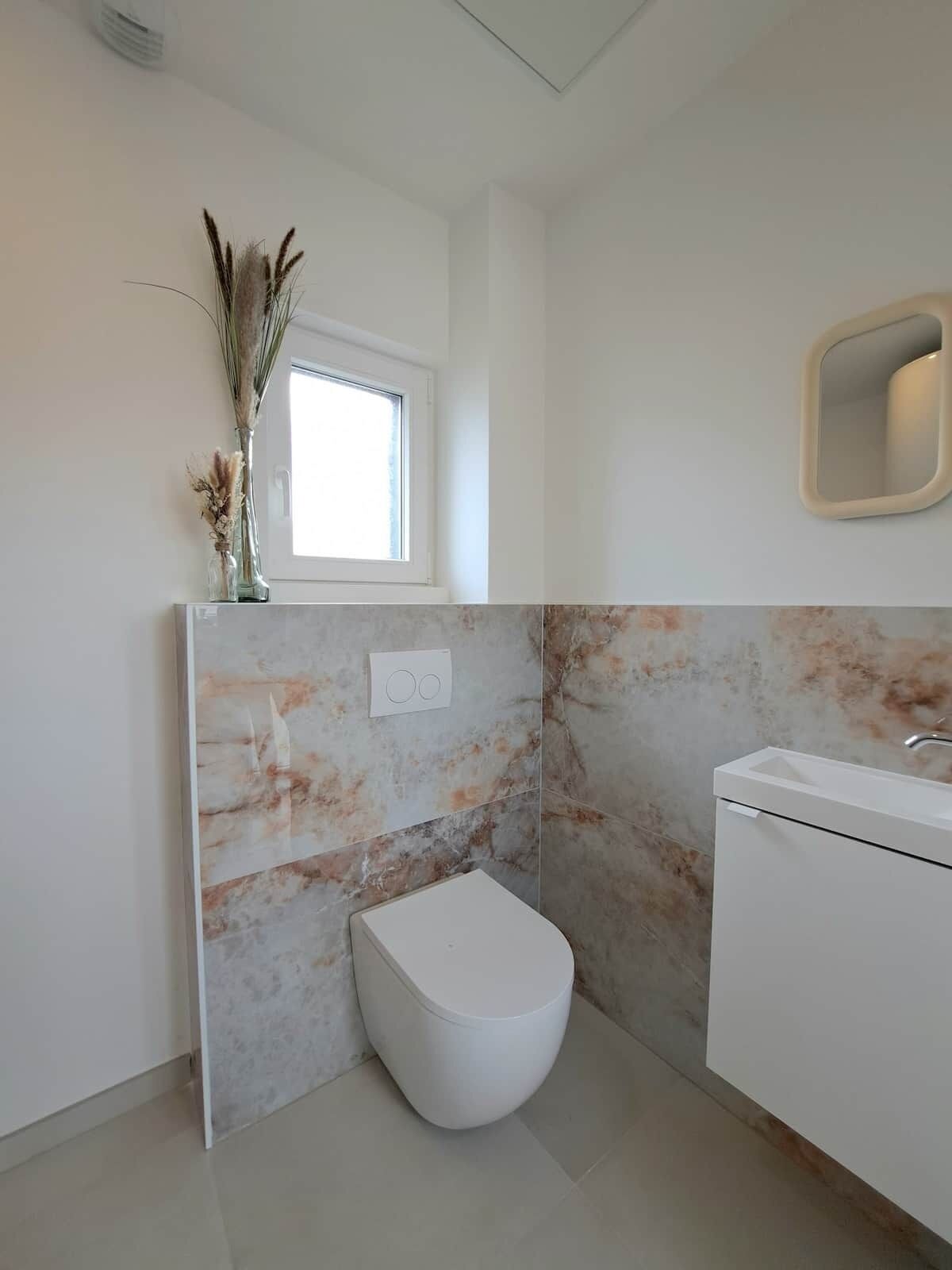 Ein modernes Badezimmer mit Toilette, Waschbecken und einem Fenster.