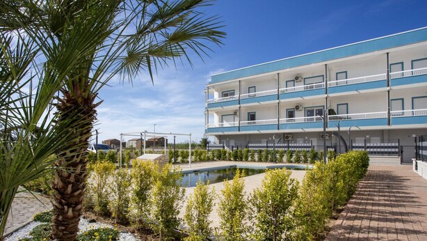 Un hotel con piscina, rodeado de vegetación y una palmera.