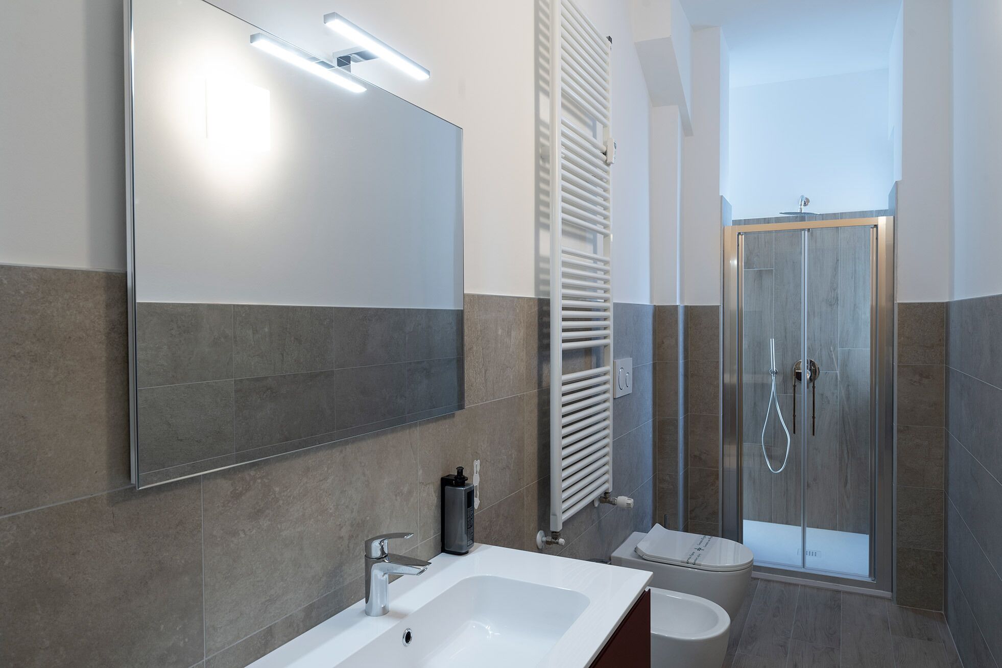 Un baño moderno con un espejo grande, un lavamanos blanco, cabina de ducha y un perchero para toallas.