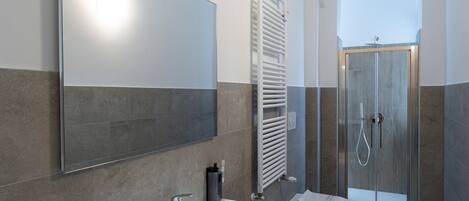 Un baño moderno con un espejo grande, un lavamanos blanco, cabina de ducha y un perchero para toallas.
