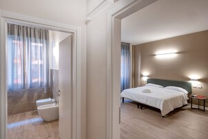 Camera d'albergo con un letto, comodino e vista all'esterno attraverso una finestra con tende.