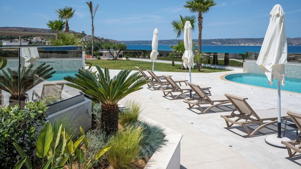 A poolside area with lounge chairs and umbrellas, a clear view of the sea, and a landscaped garden. - AmphiMatrion, Kriti penthouse luxury apartment, w/ hot tub and Sea View (C5XG+MHV Kalyves, Greece)