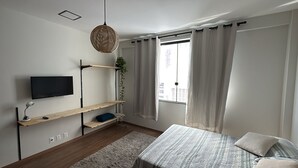 A modern bedroom with a bed, a TV mounted on the wall, wooden shelves, and a window with curtains. - Stylish Loft in Salvador's Historic Center – Walk to Pelourinho (Salvador)